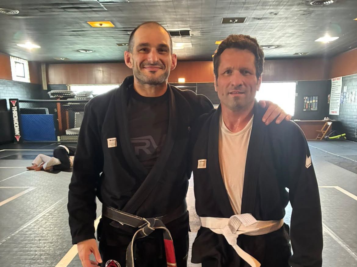 Professor Lou with a smiling adult white belt student on the academy mats